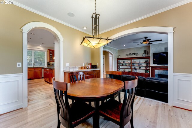 dining space with crown molding, light hardwood / wood-style floors, a tile fireplace, and ceiling fan