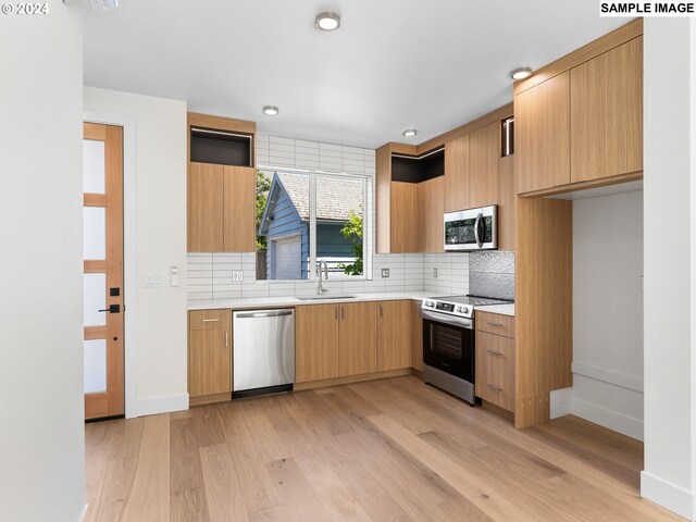 kitchen with sink, light wood-type flooring, stainless steel appliances, and backsplash