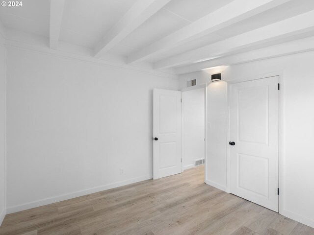 unfurnished bedroom with beam ceiling and light hardwood / wood-style floors