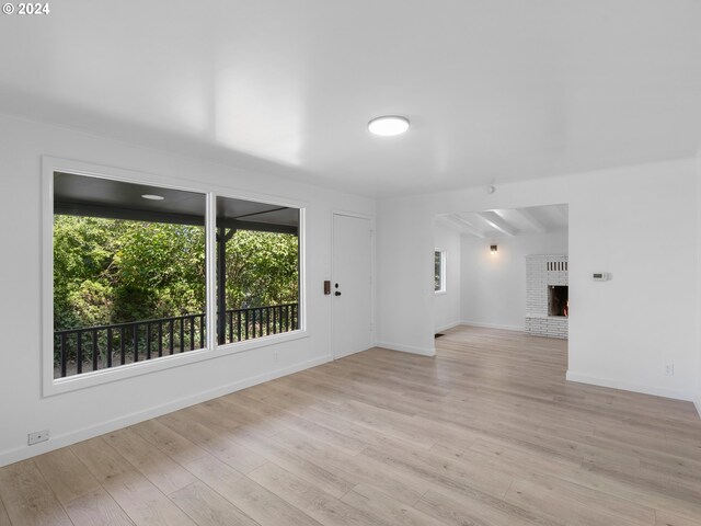 spare room featuring a brick fireplace, beamed ceiling, and light hardwood / wood-style floors