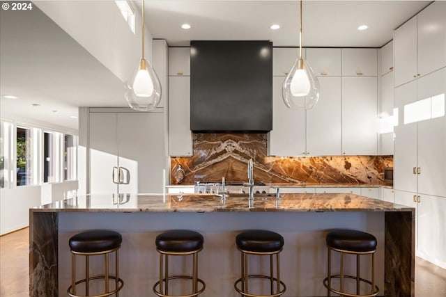 kitchen featuring a kitchen bar, sink, white cabinetry, tasteful backsplash, and dark stone countertops