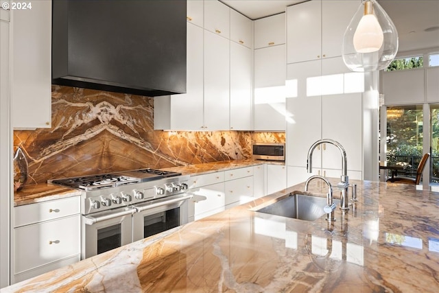 kitchen with wall chimney exhaust hood, sink, pendant lighting, stainless steel appliances, and white cabinets