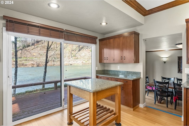 kitchen with light stone counters, ornamental molding, light hardwood / wood-style flooring, and a wealth of natural light