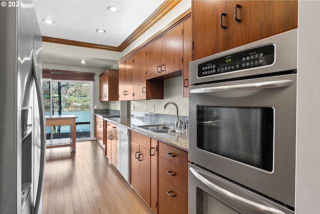 kitchen with sink, light wood-type flooring, ornamental molding, appliances with stainless steel finishes, and stone counters