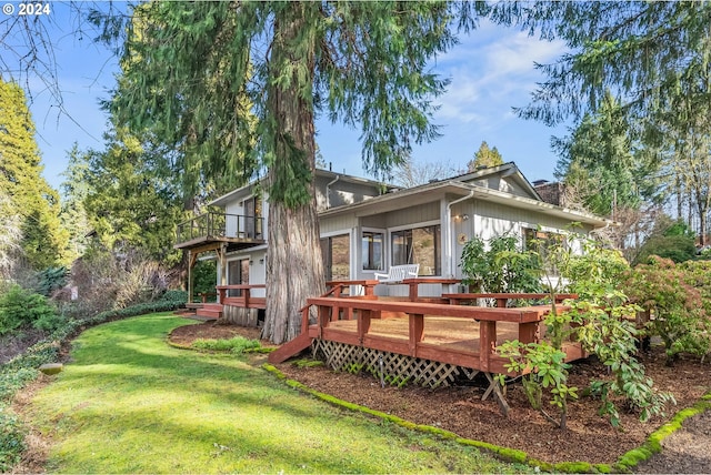 back of property with a sunroom, a deck, and a lawn