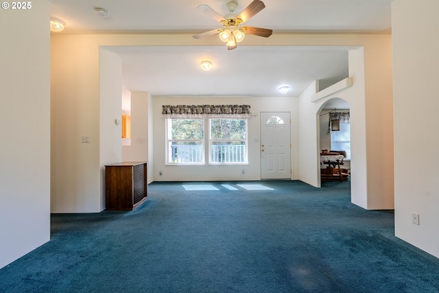 unfurnished living room with carpet, arched walkways, and a ceiling fan