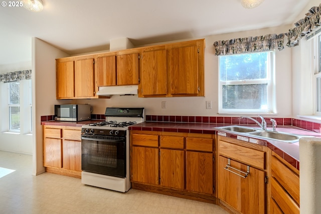 kitchen with under cabinet range hood, gas range oven, a sink, light floors, and stainless steel microwave