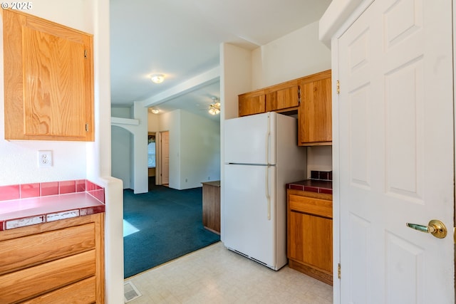 kitchen featuring brown cabinets, light floors, light colored carpet, a ceiling fan, and freestanding refrigerator