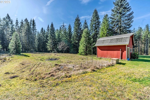 view of yard with a barn, a forest view, and an outbuilding