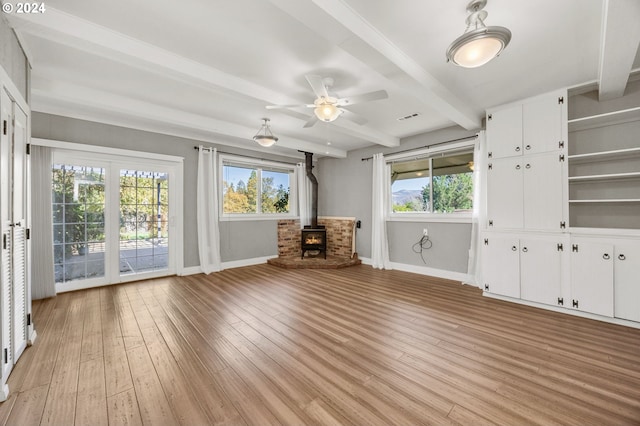 unfurnished living room featuring beam ceiling, a wood stove, plenty of natural light, and light hardwood / wood-style floors