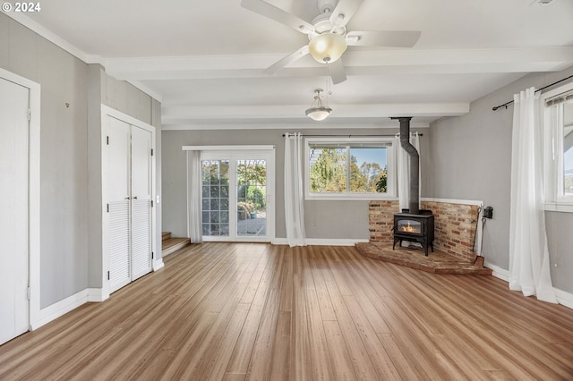 unfurnished living room featuring beamed ceiling, ceiling fan, a wood stove, and light hardwood / wood-style flooring