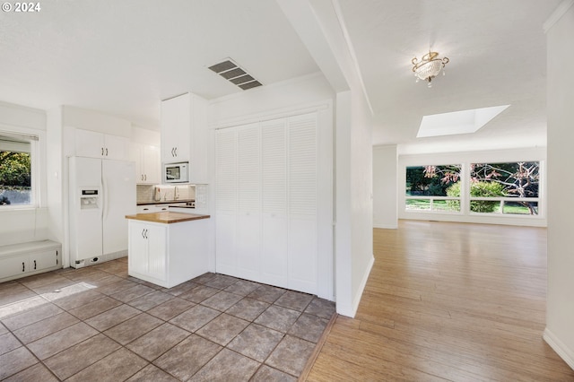 kitchen with a skylight, white cabinetry, white appliances, decorative backsplash, and light wood-type flooring