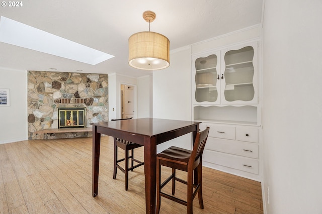 dining space with hardwood / wood-style flooring, a stone fireplace, crown molding, and a skylight