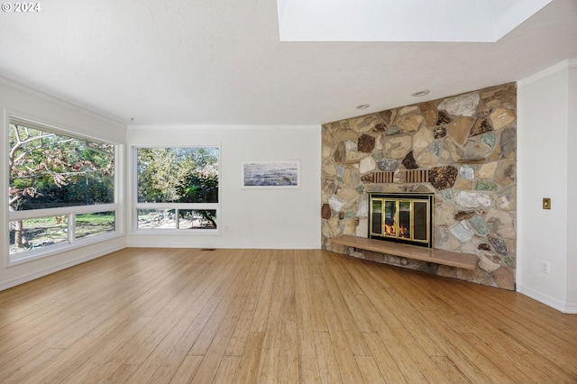 unfurnished living room featuring a stone fireplace, ornamental molding, and light wood-type flooring