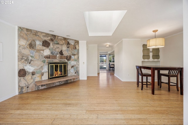 living room with a stone fireplace, light wood-type flooring, crown molding, and a skylight