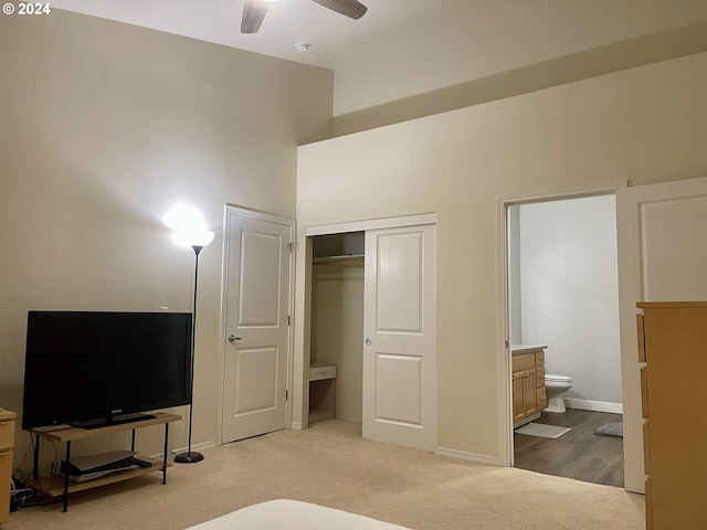 bedroom with a closet, light colored carpet, ensuite bath, and ceiling fan