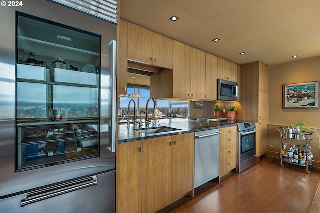 kitchen with appliances with stainless steel finishes, dark hardwood / wood-style flooring, dark stone counters, and sink