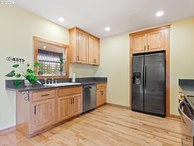 kitchen with dark countertops, light wood finished floors, light brown cabinets, appliances with stainless steel finishes, and a sink