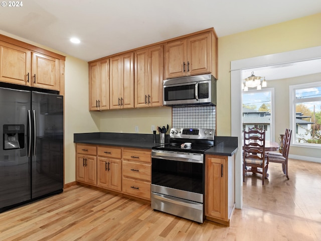 kitchen with baseboards, light wood-style floors, appliances with stainless steel finishes, dark countertops, and tasteful backsplash