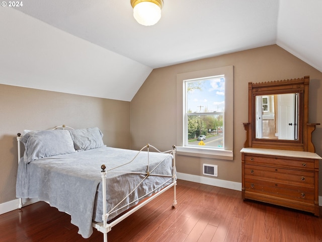 bedroom featuring vaulted ceiling, visible vents, baseboards, and wood finished floors