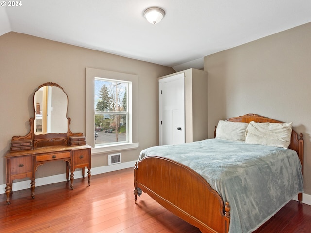 bedroom with lofted ceiling, wood finished floors, baseboards, and visible vents