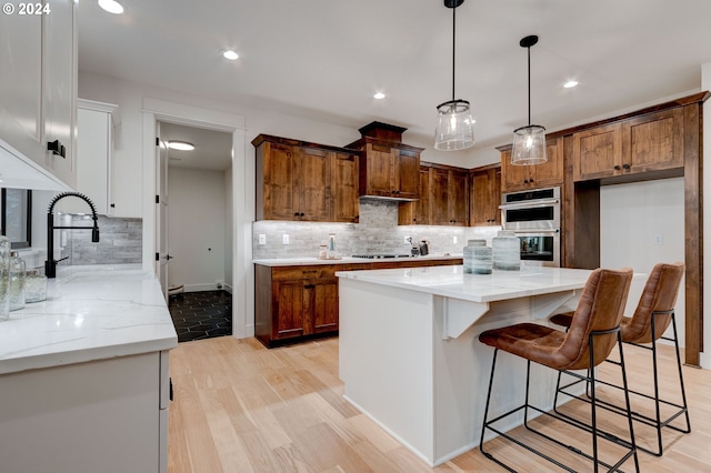 kitchen with light stone counters, decorative light fixtures, a center island, double oven, and light hardwood / wood-style floors