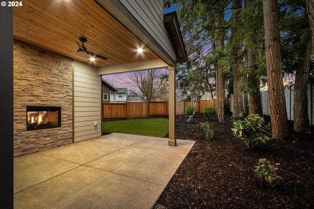 patio terrace at dusk with ceiling fan and a yard