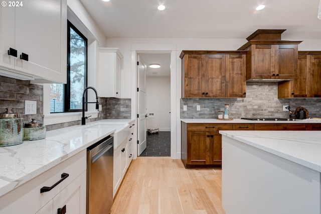 kitchen with light stone countertops, stainless steel dishwasher, white cabinets, and light wood-type flooring