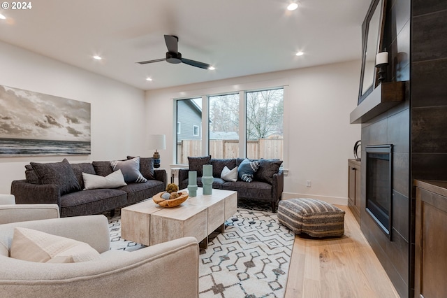 living room with a tiled fireplace, ceiling fan, and light wood-type flooring