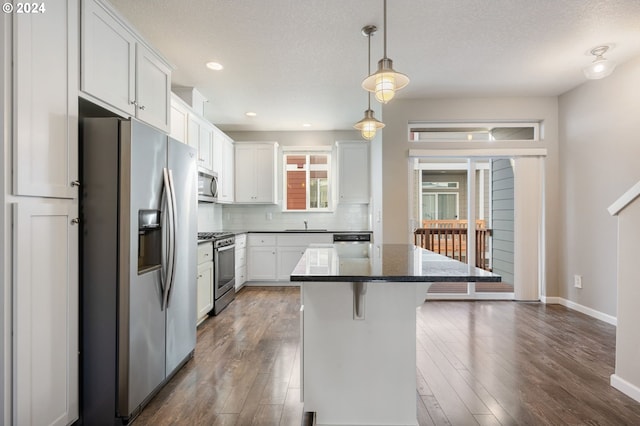 kitchen featuring a kitchen breakfast bar, hanging light fixtures, appliances with stainless steel finishes, a kitchen island, and white cabinetry