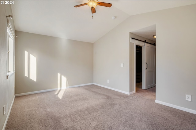 spare room with ceiling fan, a barn door, lofted ceiling, and light carpet