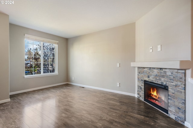 unfurnished living room with dark hardwood / wood-style floors and a stone fireplace