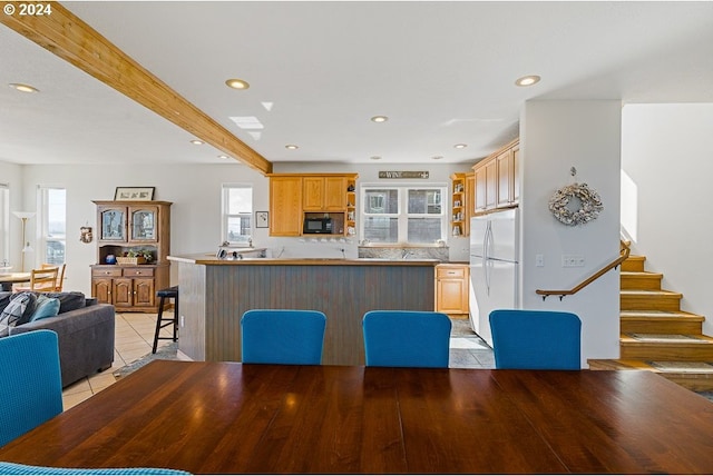 kitchen featuring beam ceiling, a kitchen breakfast bar, kitchen peninsula, white fridge, and light tile patterned floors