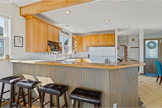 kitchen with white refrigerator, kitchen peninsula, a breakfast bar, and a healthy amount of sunlight