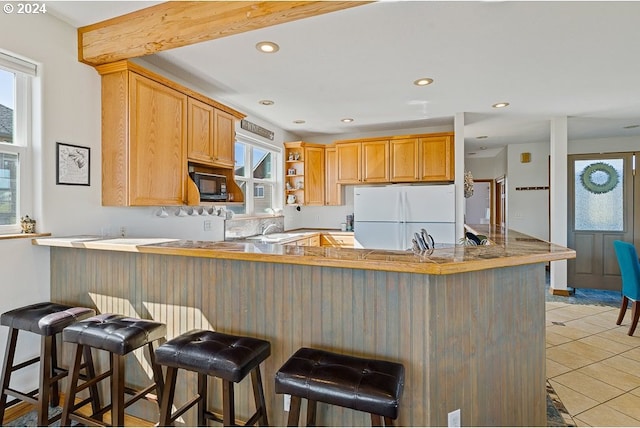 kitchen featuring recessed lighting, black microwave, light tile patterned floors, a peninsula, and freestanding refrigerator