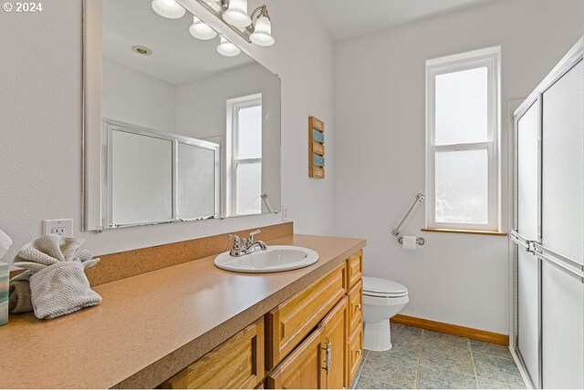 bathroom with toilet, baseboards, a shower stall, and vanity