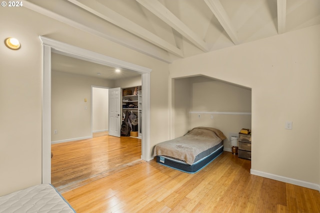 bedroom with a spacious closet, wood-type flooring, beamed ceiling, and a closet