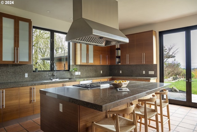 kitchen featuring a breakfast bar area, island range hood, tasteful backsplash, and sink