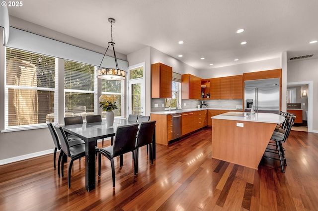 kitchen with an island with sink, decorative light fixtures, stainless steel appliances, light countertops, and open shelves