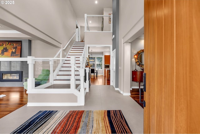 entryway with baseboards, a towering ceiling, stairway, wood finished floors, and a fireplace