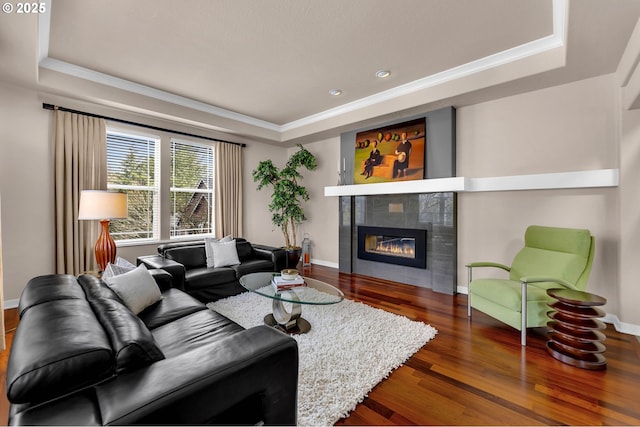 living room with dark wood-style floors, a raised ceiling, baseboards, and a tiled fireplace