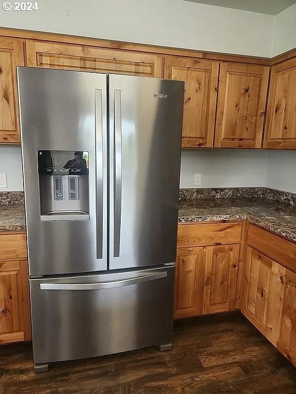 kitchen with dark hardwood / wood-style flooring, dark stone counters, and stainless steel fridge with ice dispenser