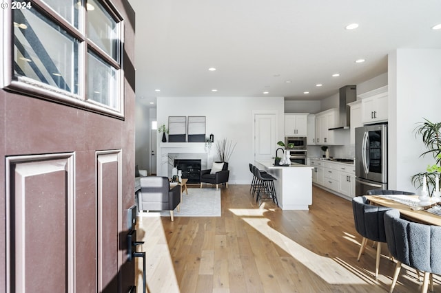 kitchen with a kitchen bar, appliances with stainless steel finishes, light wood-type flooring, white cabinets, and an island with sink