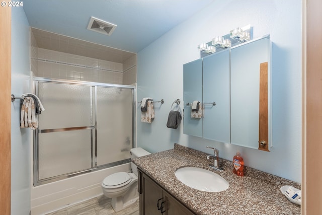 full bathroom with bath / shower combo with glass door, toilet, and vanity