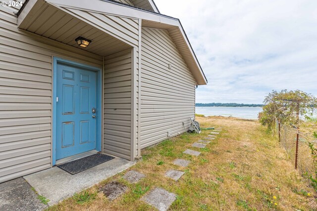 view of exterior entry featuring a water view and a lawn