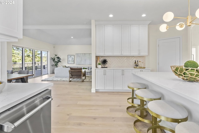 kitchen with a breakfast bar, white cabinetry, stainless steel dishwasher, light hardwood / wood-style flooring, and pendant lighting