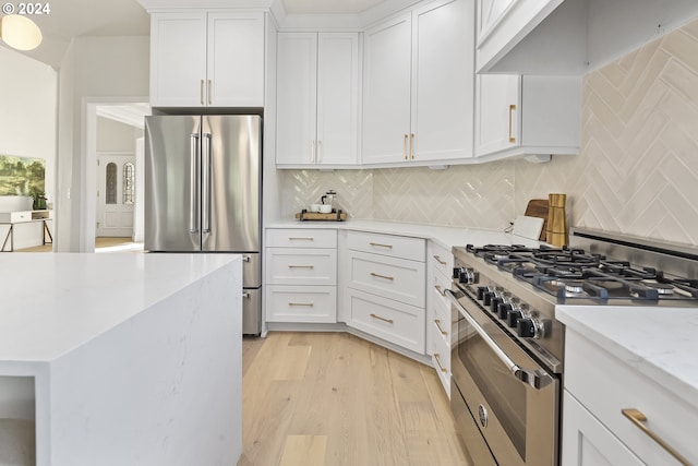 kitchen with backsplash, light stone countertops, high quality appliances, white cabinetry, and light wood-type flooring