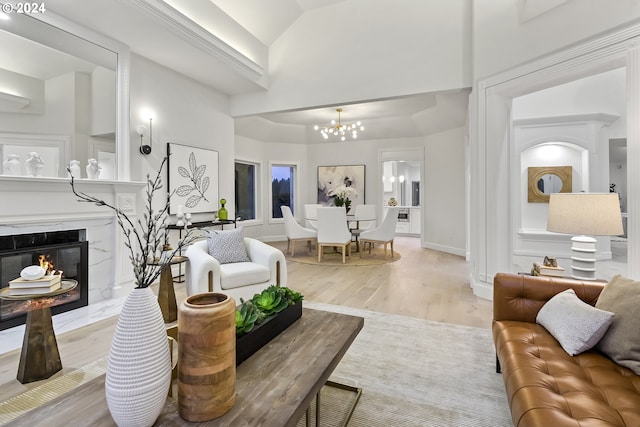 living room featuring a chandelier, a high end fireplace, a high ceiling, and light wood-type flooring