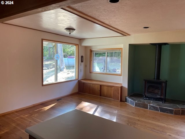 unfurnished living room with a textured ceiling, wood-type flooring, and a wood stove