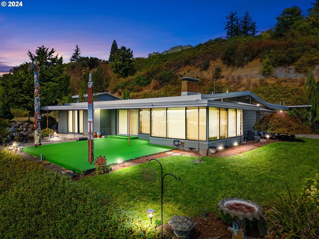 back house at dusk featuring a lawn